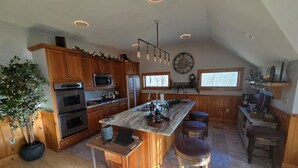 A spacious kitchen with wooden cabinets, a large island with stools, and a central island with a sink and bar area. - The Jefferson Guest House, Spacious, Special Views (Litchfield)