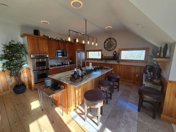 A spacious kitchen with wooden cabinets, a large island with stools, and a clock on the wall.