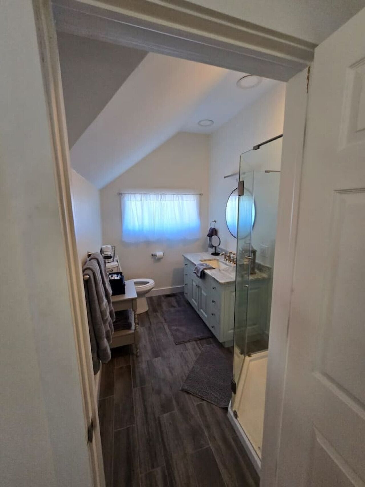 A narrow, sloped ceiling bathroom with a toilet, sink, and mirror.