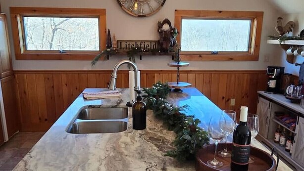 A kitchen with a marble island, wooden cabinets, a clock, and a window with a view of trees. - The Jefferson Guest House, Spacious, Special Views (Litchfield)
