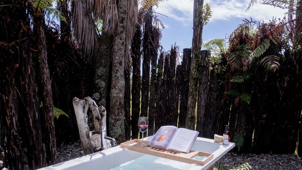 Un jacuzzi con un libro y una copa de vino, rodeado de árboles y una terraza de madera.