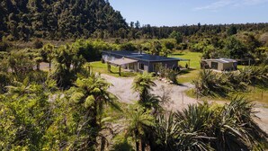 Una casa moderna con un amplio techo de paneles solares, rodeada de exuberante vegetación y una ladera boscosa.