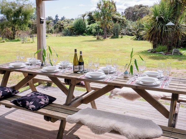 Un juego de mesa de picnic de madera al aire libre con platos, vasos y botellas de vino.