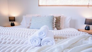 Una cama bien hecha con toallas blancas enrolladas, una manta suave y almohadas decorativas.