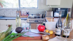 Una encimera de cocina con ingredientes para cocinar, una tabla de cortar, un bol blanco y copas de vino.