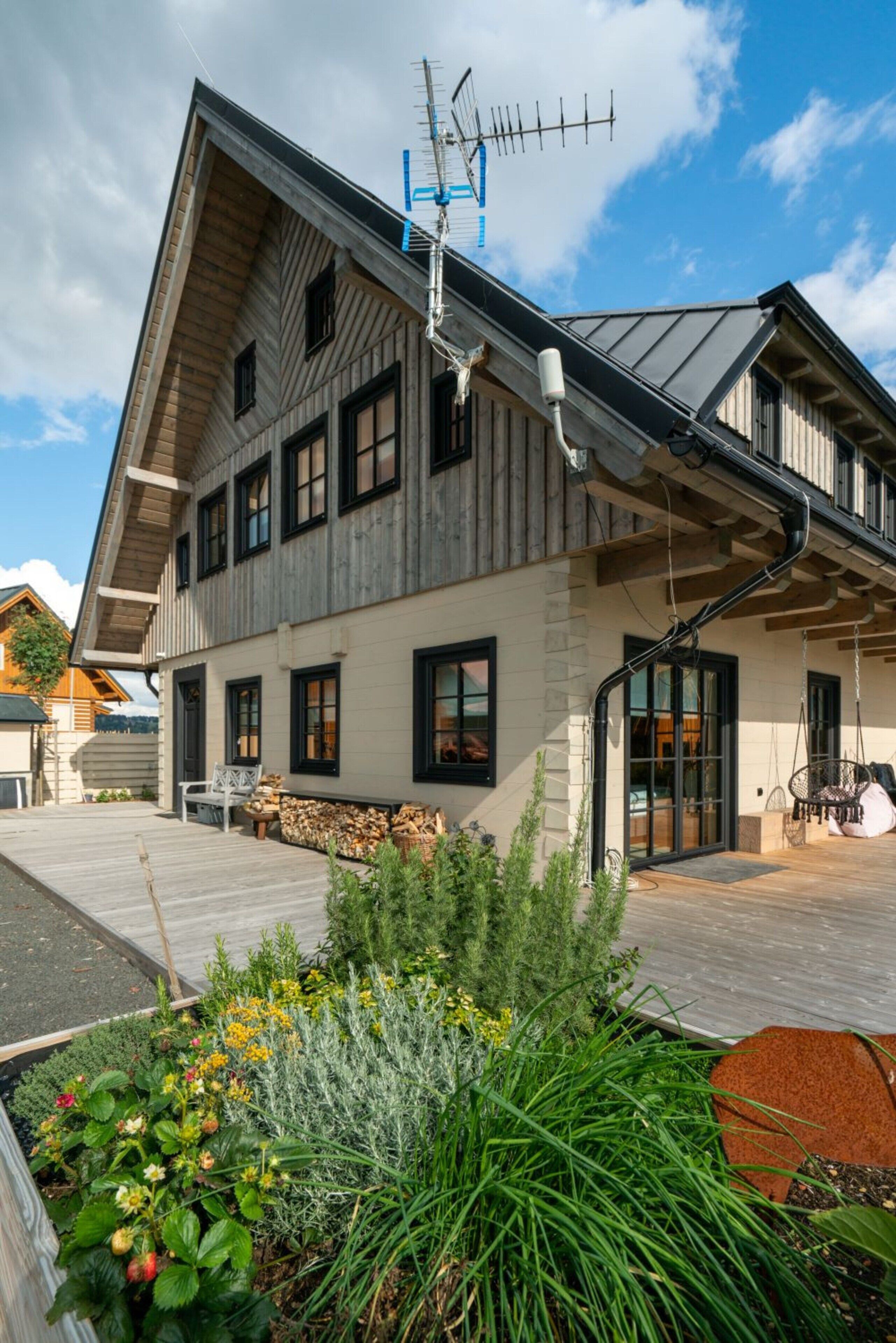 A modern house with a sloped roof, a visible chimney, and a wooden deck with outdoor seating.