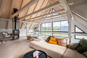 Un loft espaiós amb un sostre alt, un sofà acollidor, una llar de foc i grans finestres que ofereixen vistes a l'exterior.