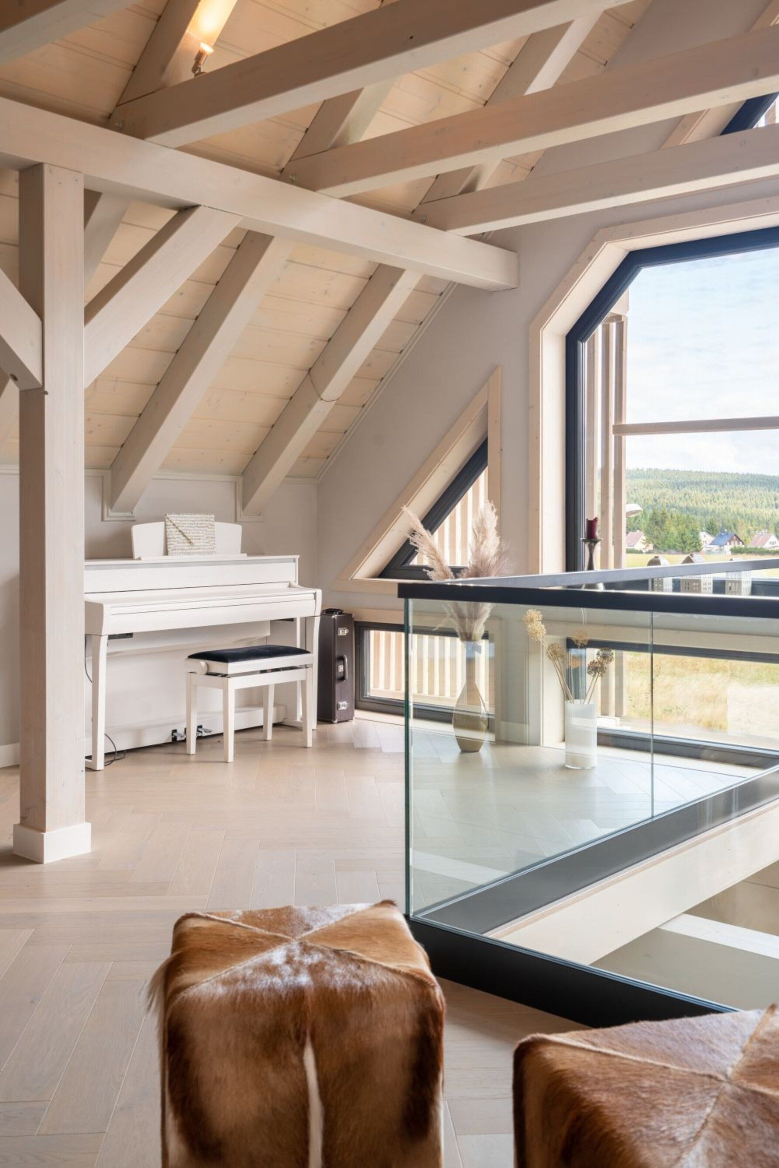A spacious loft with a piano, a glass railing overlooking a scenic view, and a large window.