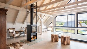 A spacious loft with high ceilings, exposed wooden beams, a fireplace, and large windows offering a view of the outdoors. - Villa in Abertamy Near Klinovec Ski Resort (Abertamy)