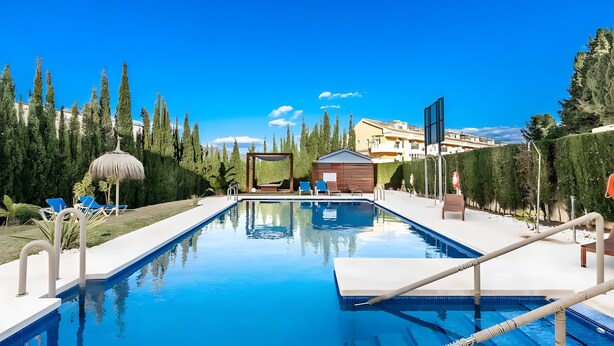 A swimming pool with lounge chairs, a wooden hut, and a clear blue sky. - Elegant Apartment in a Prime Location (Marbella)