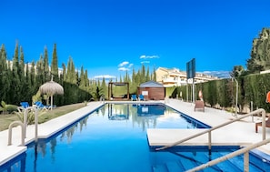 A swimming pool with lounge chairs, a wooden hut, and a clear blue sky. - Elegant Apartment in a Prime Location (Marbella)