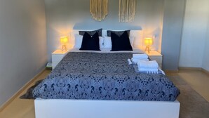 A bed with a patterned bedspread, two bedside lamps, and macramé wall hangings. - Elegant Apartment in a Prime Location (Marbella)