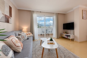 A modern living room with a sofa, a coffee table, a TV, and a balcony with a view. - Elegant Apartment in a Prime Location (Marbella)