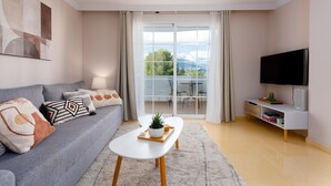 A modern living room with a grey sofa, a white coffee table, a flat-screen TV, and a balcony with a view. - Elegant Apartment in a Prime Location (Marbella)