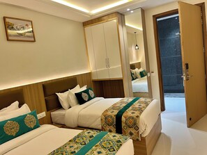 A hotel room with two beds, a wardrobe, a mirror, and a painting on the wall. - Hotel Green One Earth (Amritsar)