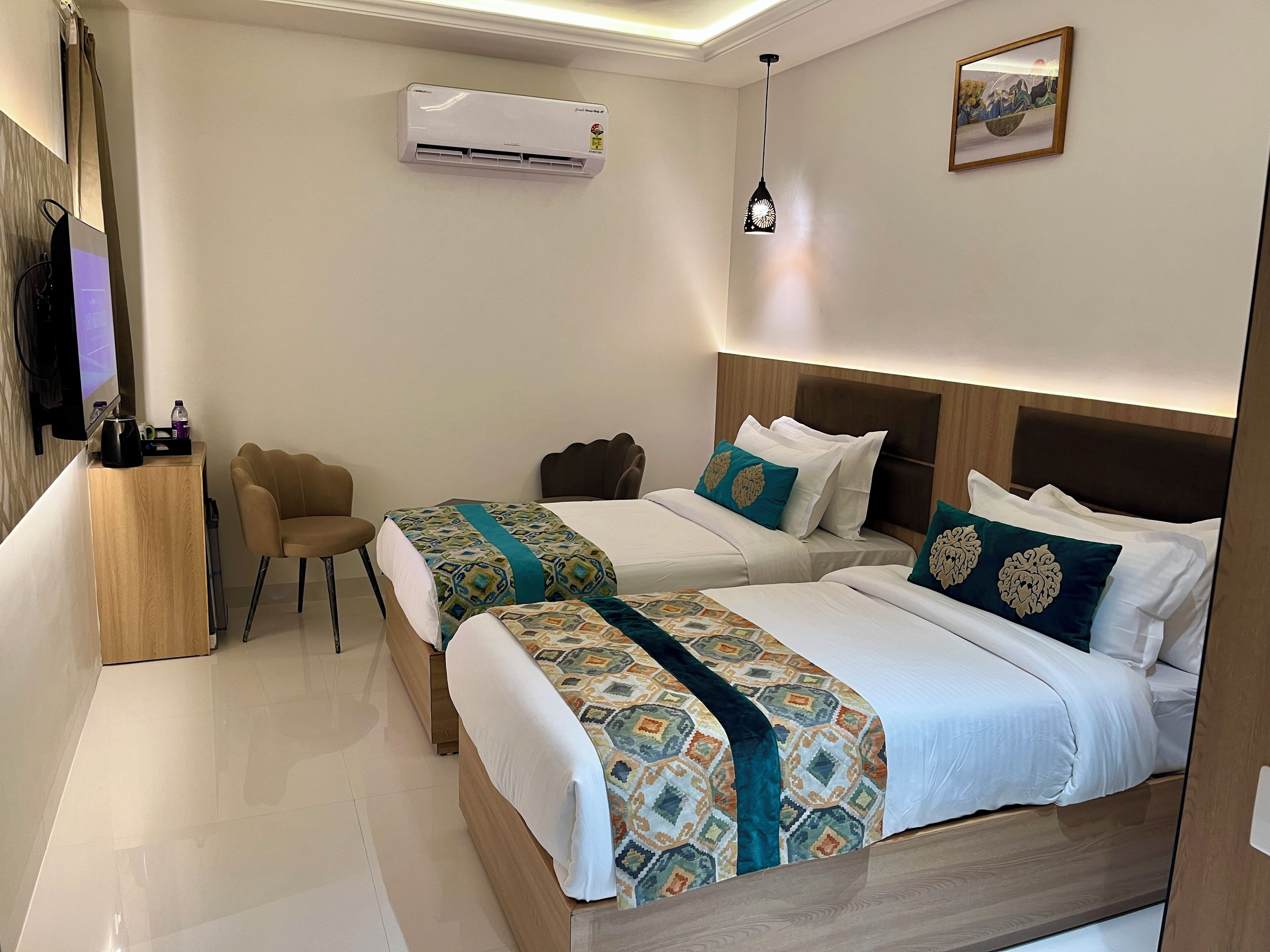 A hotel room with two beds, a TV, a desk, and an air conditioner.
