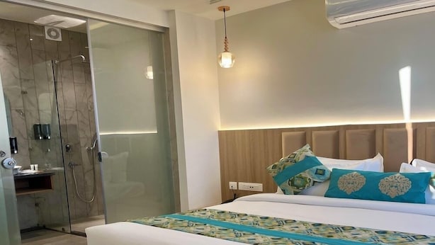 A modern hotel room with a large bed, a shower area, and an air conditioning unit. - Hotel Green One Earth (Amritsar)