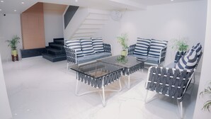 A modern living room with a glass coffee table, striped sofas, and a staircase. - Hotel Green One Earth (Amritsar)
