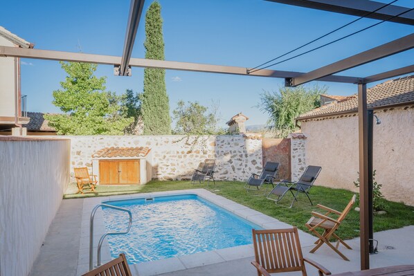 Una piscina con sillas de descanso, una pérgola y un muro de piedra.