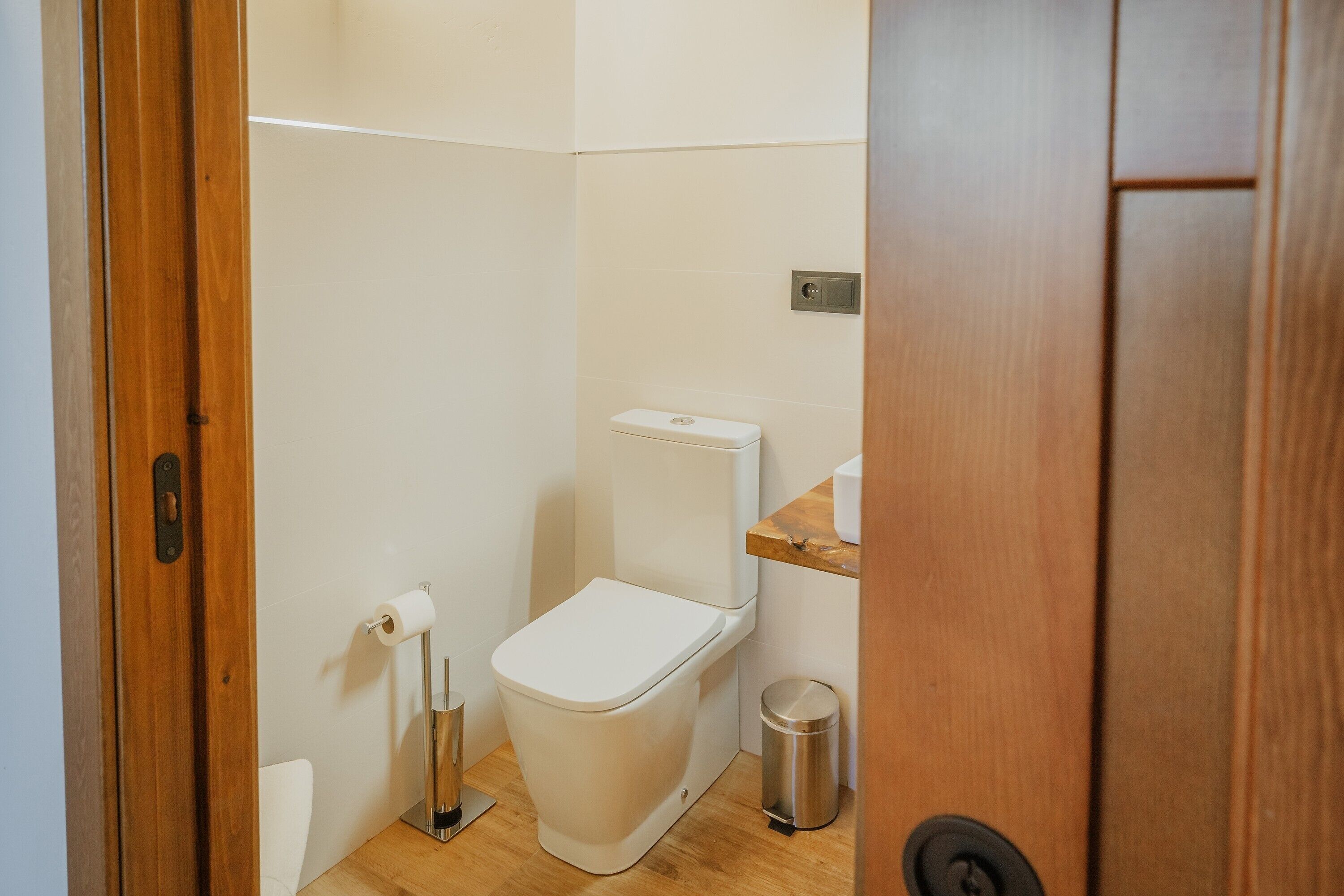 Ein kleines, sauberes Badezimmer mit Toilette, Mülleimer und Holztür.