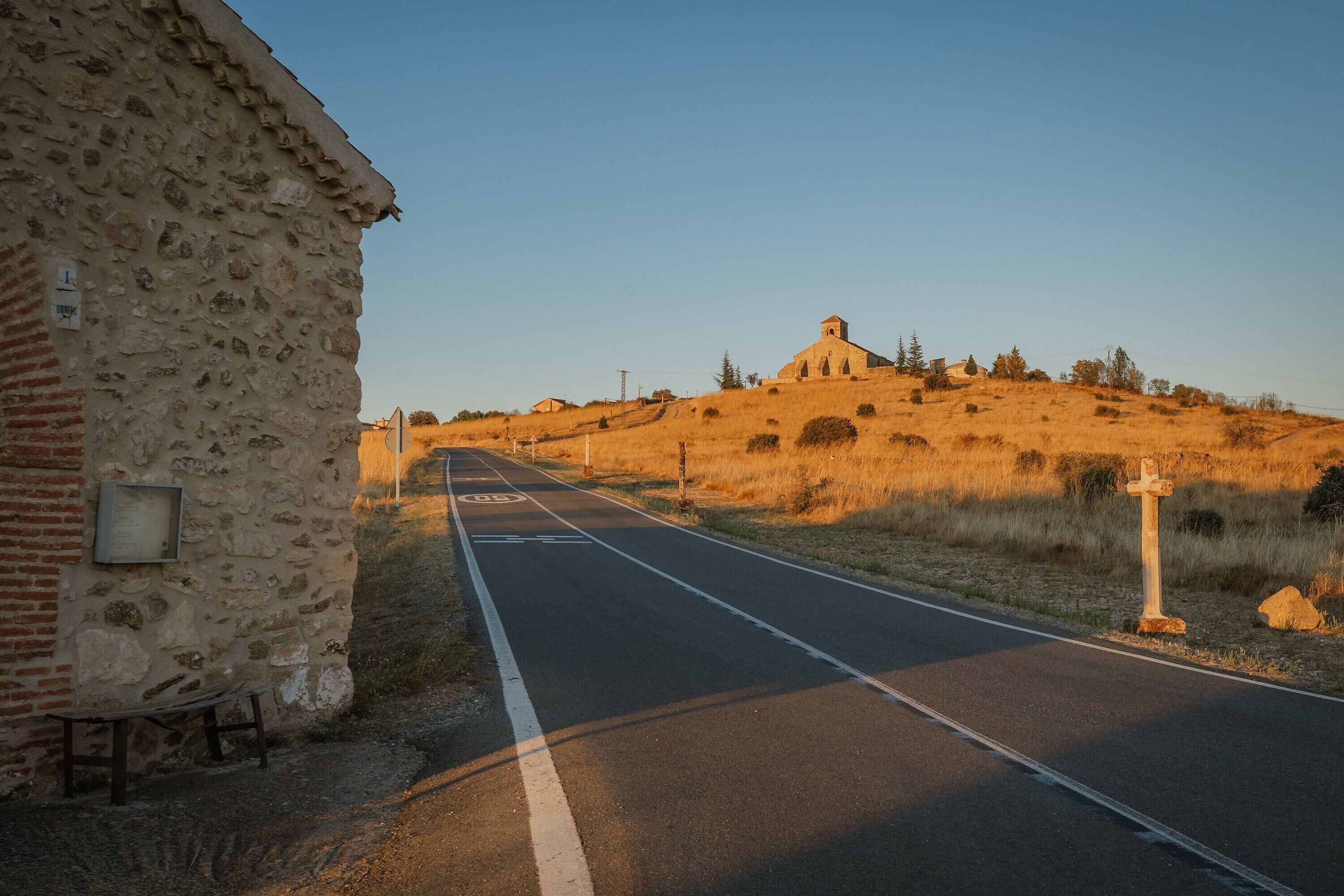 Une route menant à un bâtiment en pierre, avec une petite construction située sur une colline.