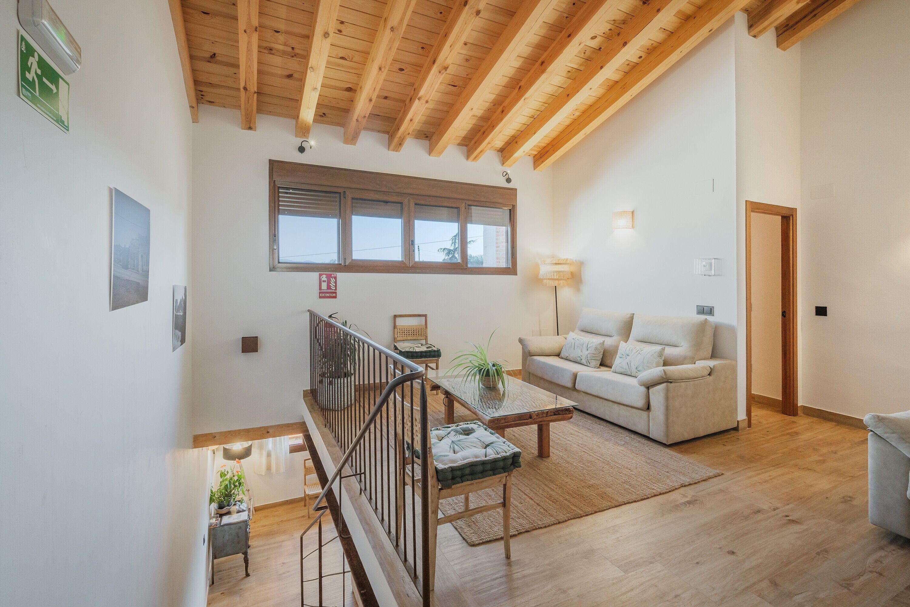 A spacious living area with a wooden ceiling, a sofa, a coffee table, and a staircase.