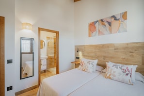 A bedroom with a wooden headboard, a bed with floral pillows, a large mirror, and a wall-mounted abstract art piece.