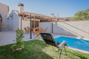 Un patio trasero con piscina, pérgola y mobiliario exterior.