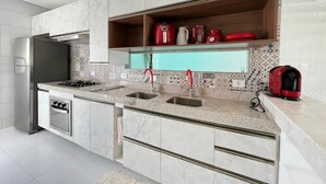 Een moderne keuken met een ingebouwde oven, een koelkast van roestvrij staal en een aanrecht met een spoelbak en een rode waterkoker.