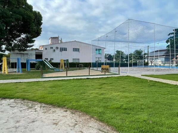 Un parque infantil con una zona amparada por red, un tobogán y un edificio al fondo.