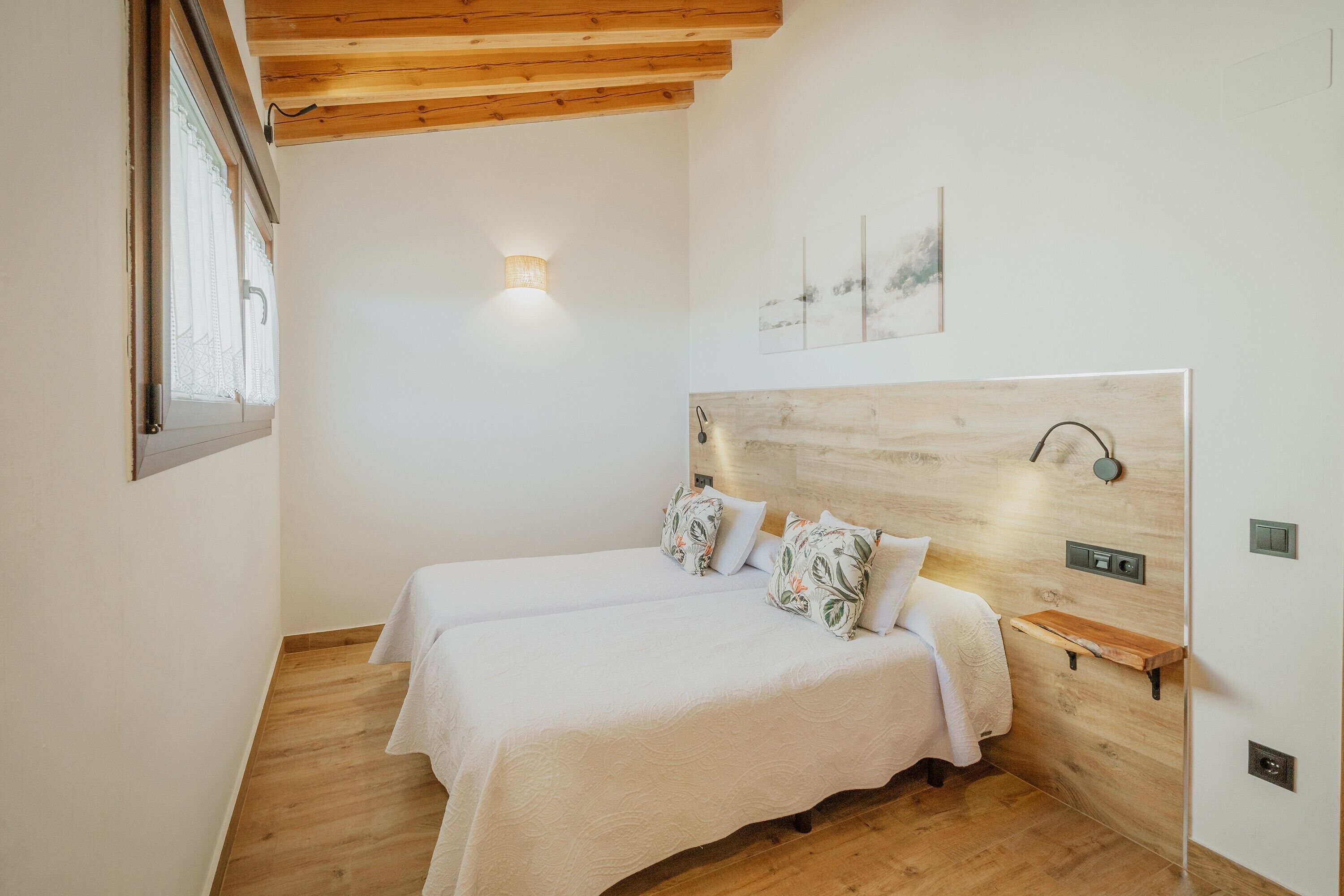 Een slaapkamer met twee bedden, een houten hoofdbord, nachtkastjes, een wandlamp en een raam.
