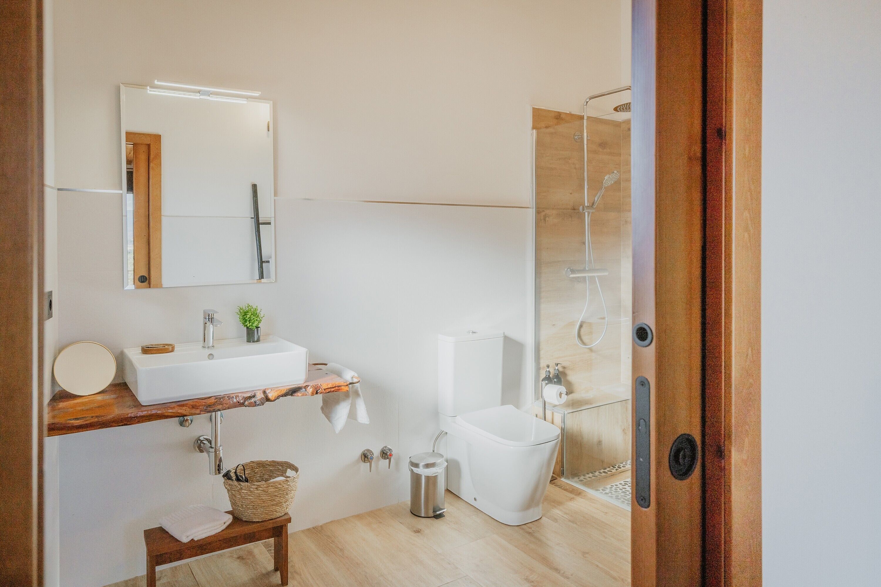 A modern bathroom with a wooden vanity, a white sink, a toilet, and a glass shower enclosure.