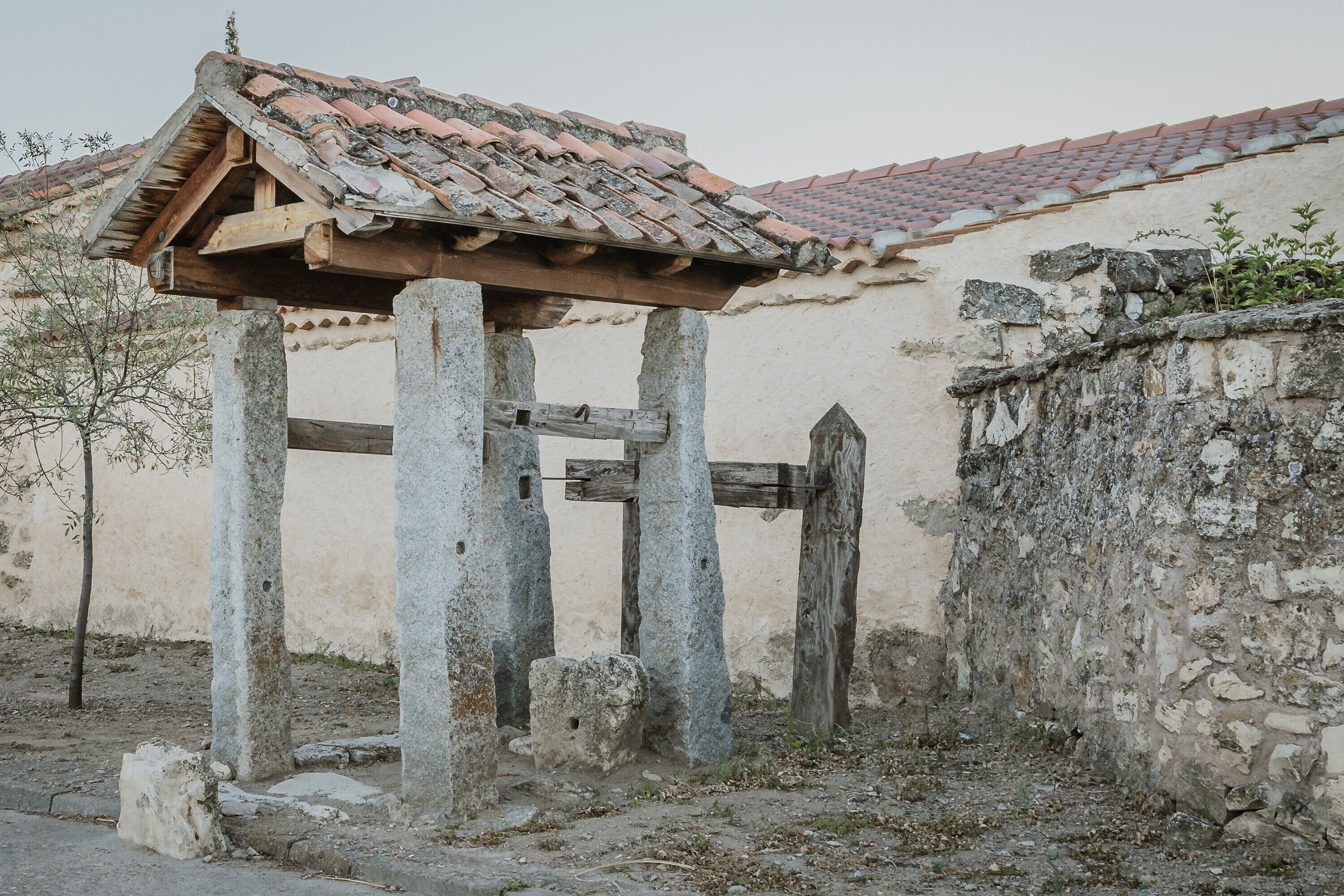 A stone structure with a tiled roof, a wooden gate, and a wall with vegetation.