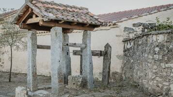 A stone structure with a tiled roof, a wooden gate, and a wall with vegetation.