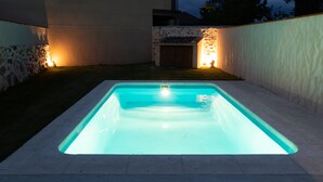 Ein rechteckiger Pool mit hellblauem Innenraum, umgeben von einer Steinsäule und einer niedrigen Mauer mit einer kleinen Lampe.