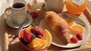 Ένα δίσκος πρωινού με κρουασάν, φράουλες, φέτες πορτοκαλιού, μια κούπα καφέ και μια κανάτα με χυμό πορτοκαλιού πάνω στο κρεβάτι.