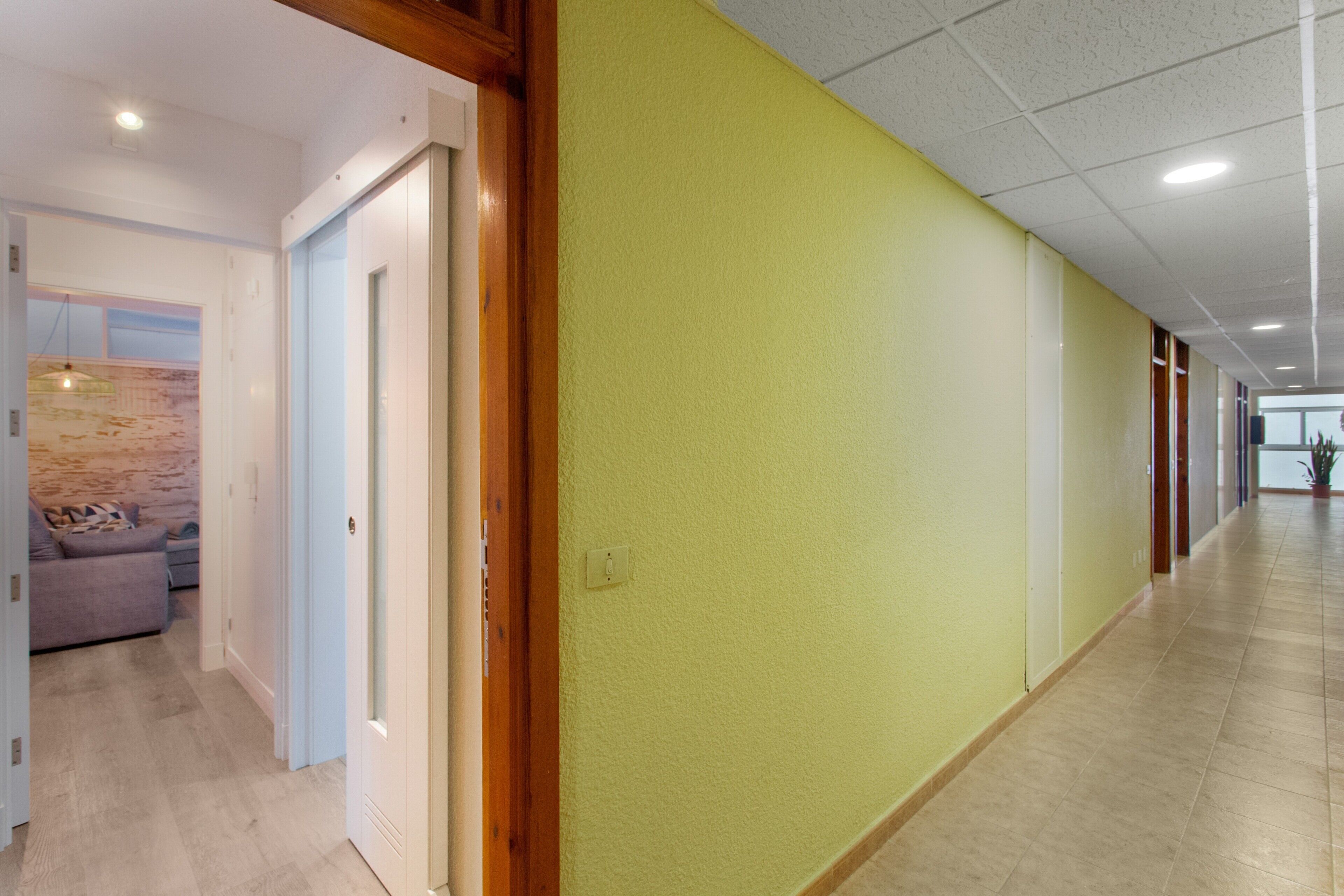 Un couloir avec un mur vert, des encadrements de porte en bois et un plancher de couleur claire.