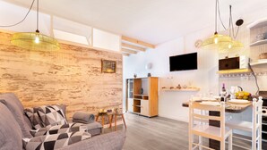 Una sala de estar moderna con sofá, mesa de comedor y sillas, una zona de cocina con televisor y una pared de acento de madera.