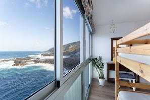 A room with a large window overlooking a rocky coastline, a wooden bunk bed, and a potted plant.