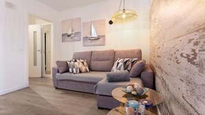 Una sala de estar con un sofá gris, una mesa de centro de vidrio y dos cuadros de veleros en la pared.