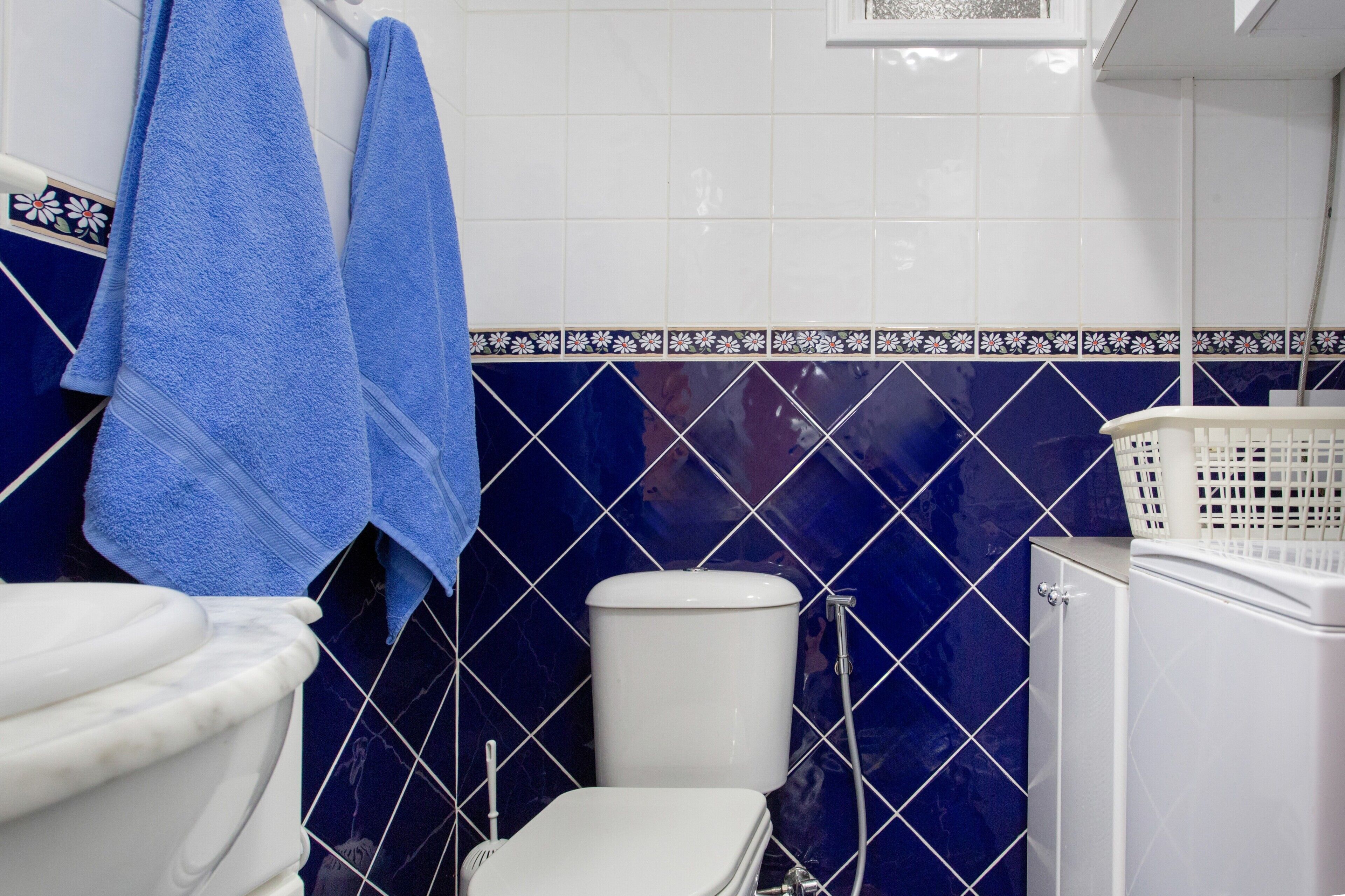 Casa de banho com sanita, máquina de lavar roupa e toalhas penduradas num suporte.