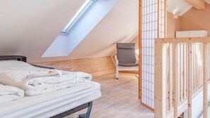Une chambre avec un plafond en pente, un puits de lumière, un lit, une chaise et une armoire en bois.