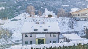 Un paysage montagneux enneigé avec un immeuble résidentiel doté d’une porte jaune, de nombreuses fenêtres et d’un toit en pente.
