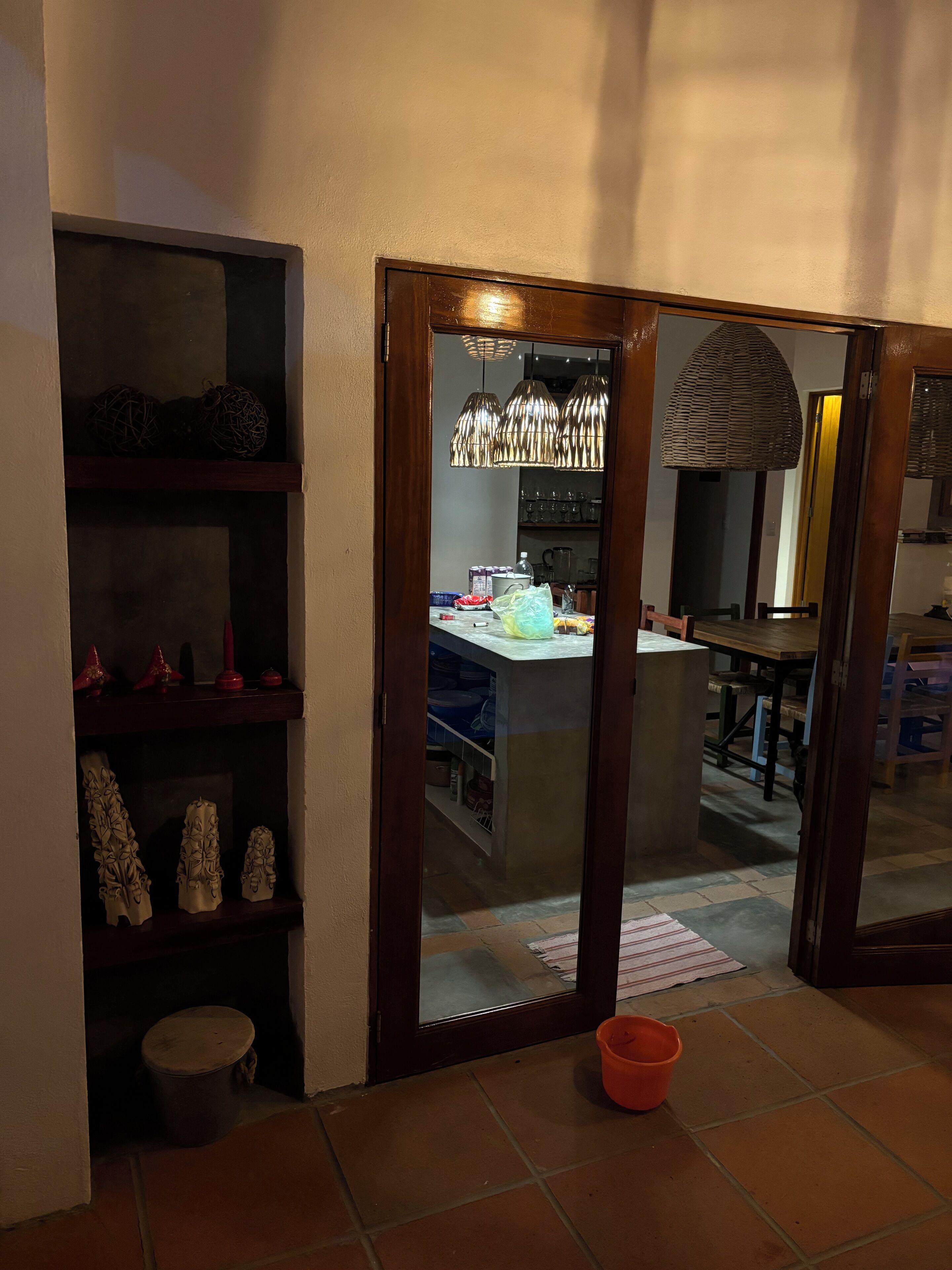 Una habitación con puerta de madera, suelo de baldosas y un cubo naranja pequeño.