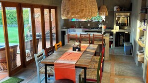 A spacious dining area with a long table, wicker pendant lights, and a view of the garden through large sliding doors. - Casa en Lomas de Cocoyoc, Alberca, Pet friendly. (Fraccionamiento Lomas de Cocoyoc)