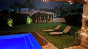 A backyard with a swimming pool, two lounge chairs, and string lights. - Casa en Lomas de Cocoyoc, Alberca, Pet friendly. (Fraccionamiento Lomas de Cocoyoc)