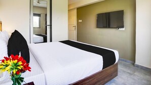 A hotel room with a bed, a TV mounted on the wall, and a door leading to a bathroom. - Vibes INN (Mumbai)