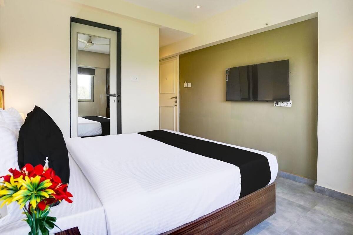 A hotel room with a bed, a TV mounted on the wall, and a door leading to a bathroom.