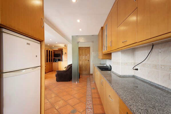 A kitchen with wooden cabinets, a refrigerator, and a tiled floor. - Apartment 'Xavega' with Sea View, Private Terrace and Balcony (Torreira)