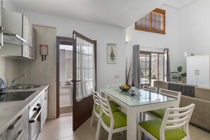 A modern kitchen with a glass dining table, white chairs, and a beige sofa.